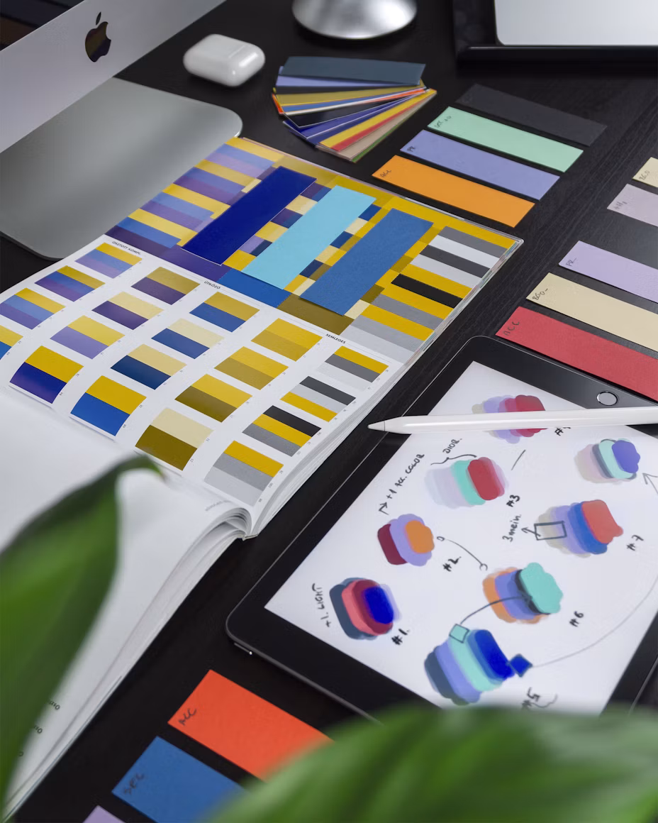 Mesa de trabajo con composiciones gráficas, muestras de color y una tableta con estudios visuales